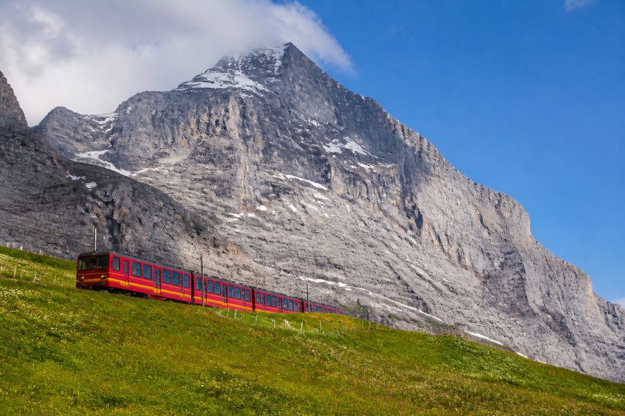 Tren rojo de cremallera subiendo por un prado alpino, con la pared del Eiger detrás