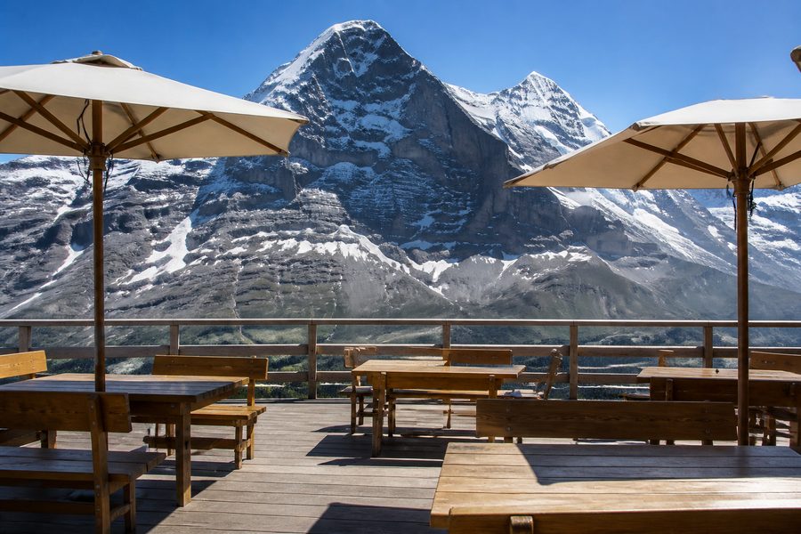 Terraza de restaurante de montaña con mesas de madera frente a la pared norte del Eiger