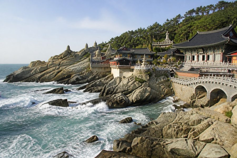 El templo Haedong Yonggungsa sobre las rocas junto al mar, con las olas rompiendo bajo sus pabellones