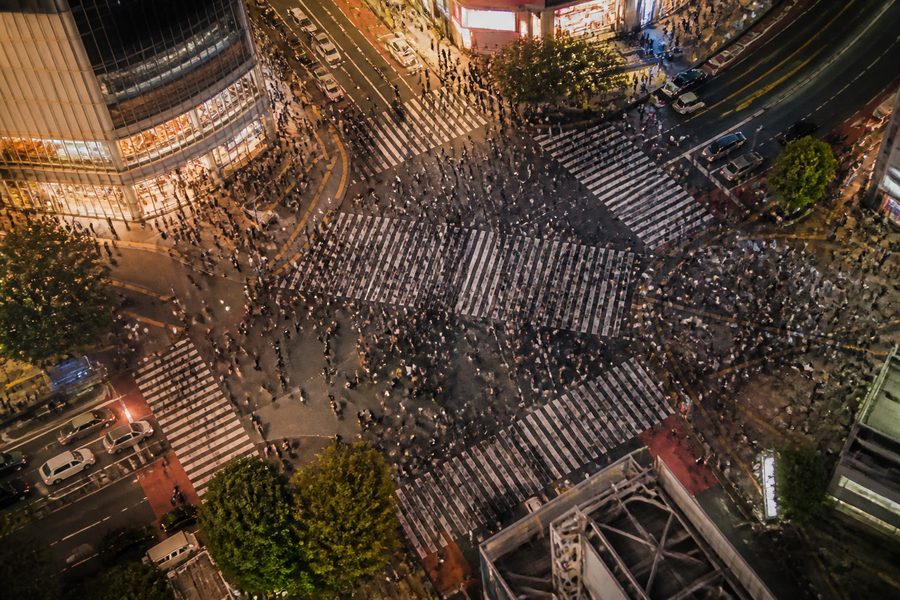 El cruce de Shibuya visto desde arriba al anochecer, con cientos de peatones atravesándolo y las pantallas de los edificios encendidas