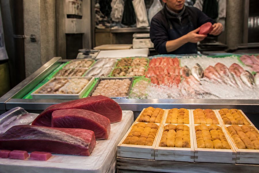 Puesto de pescado y marisco sobre hielo en el mercado exterior de Tsukiji, con el vendedor detrás del mostrador