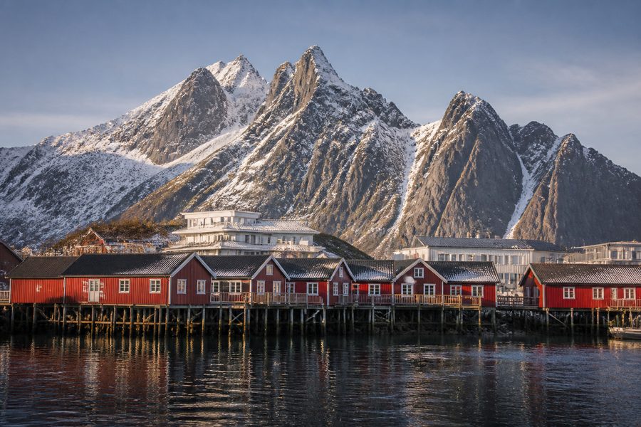 Casas rojas de pescadores sobre el agua en el puerto de Svolvaer, con picos escarpados nevados detras
