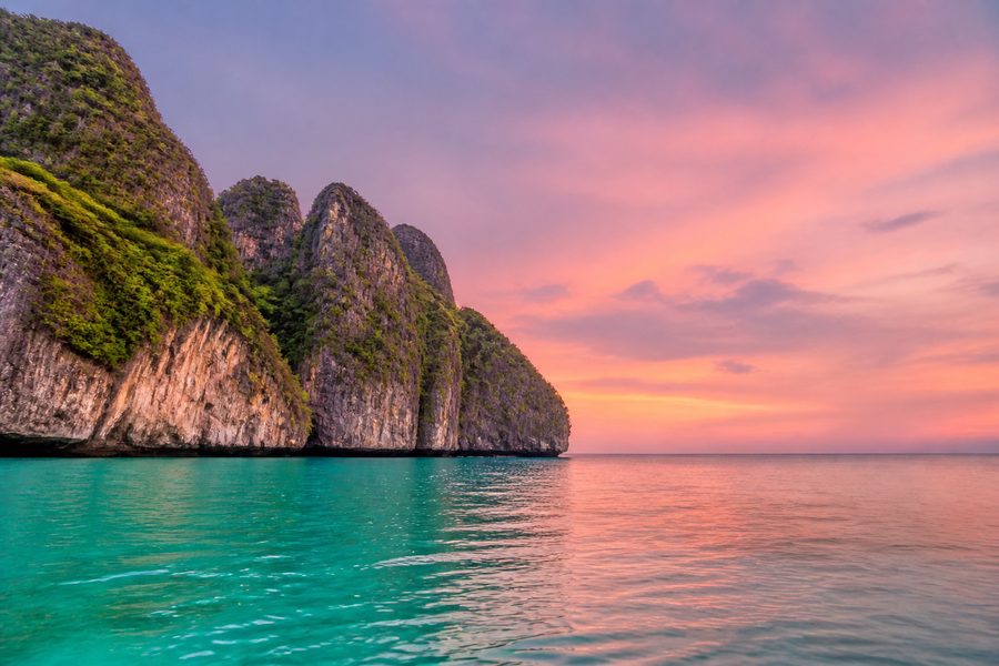 Acantilados de roca caliza emergiendo de un mar en calma al amanecer, con el cielo rosado
