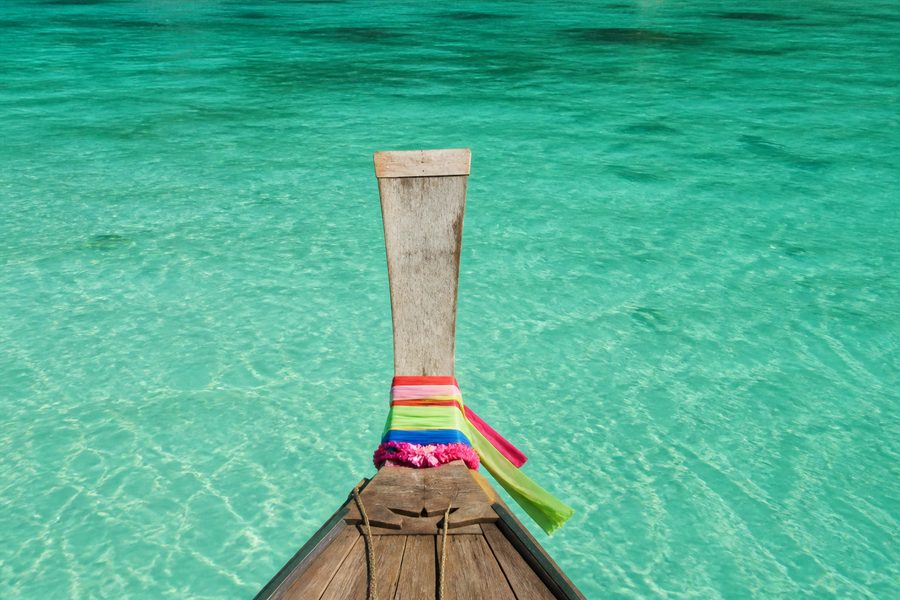 Proa de una barca de cola larga tailandesa con cintas de colores, sobre agua turquesa transparente